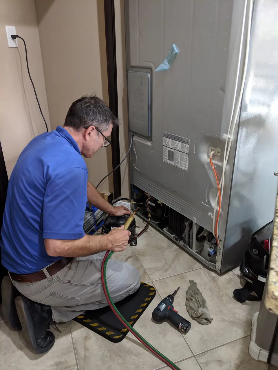 A technician working at the back of a refrigerator with the service area exposed