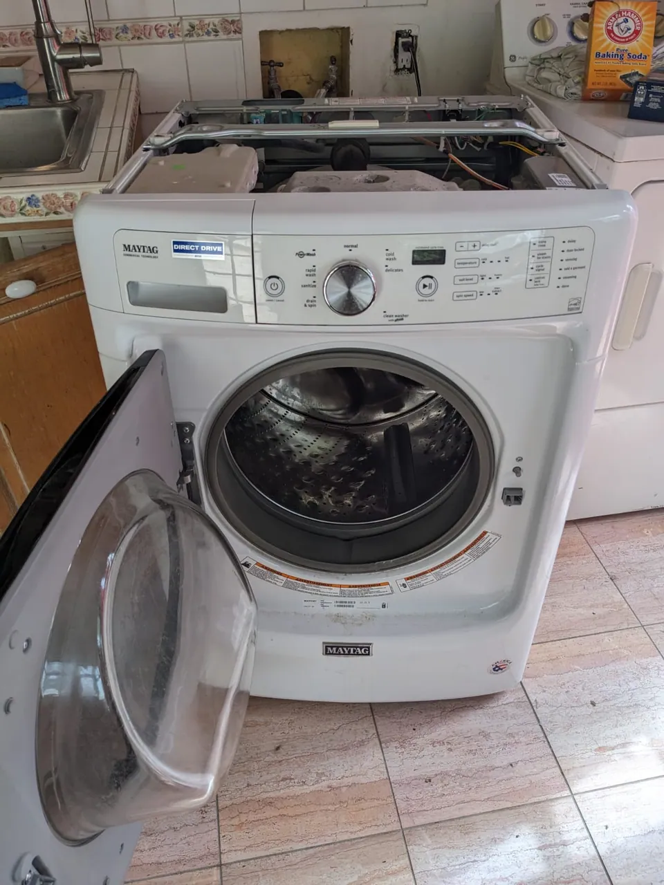 A front-loading washing machine opened for service in a laundry room